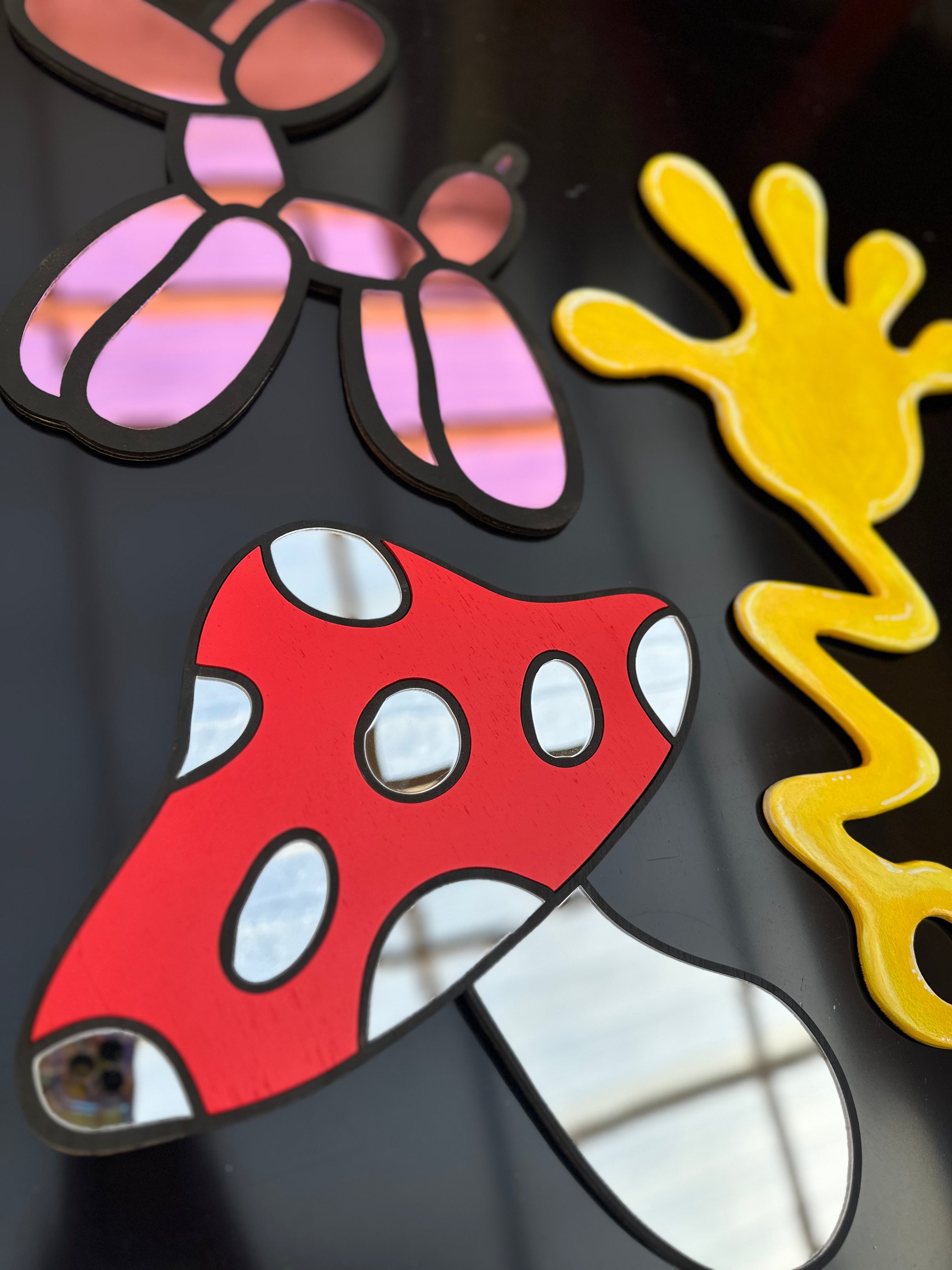 Colorful abstract design with a red mushroom-like shape, pink flower, and yellow sun on a black background.